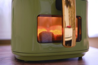 Golden-brown chicken nuggets are cooking in an air fryer, with a warm glow visible through the