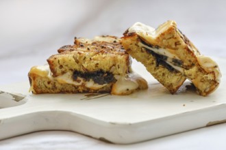 A delicious three cheese sandwich sits on a wooden cutting board, showcasing a golden-brown crust.