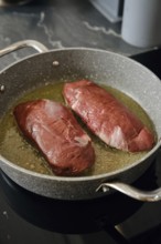Two duck breasts are sizzling in a pan with hot fat, infusing the kitchen with rich aroma