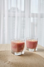 Two elegant glasses filled with a vibrant banana-strawberry smoothie sit atop a woven placemat on a