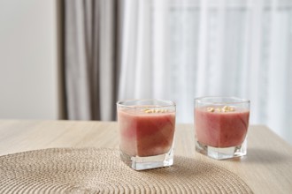Two glasses filled with a vibrant banana-strawberry smoothie are placed on a light wooden table