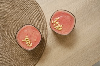 Two glasses filled with a creamy banana-strawberry smoothie sit on a natural-colored table. Topped