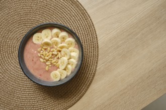 Bright and colorful banana strawberry smoothie is topped with fresh banana slices and pine nuts,