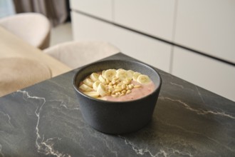 Bright and inviting banana-strawberry smoothie sits in a dark bowl, garnished with fresh banana