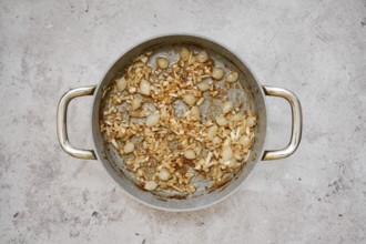 A silver pan contains a mixture of caramelized pearl onions and chopped shallot, creating a savory