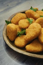Close-up view of golden-brown chicken nuggets in breading on a rustic wooden platter. The crispy