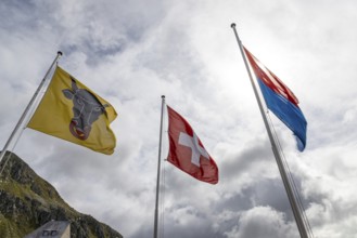Flags of the cantons of Uri and Ticino and the Swiss flag waving in the wind, Gotthard Pass,