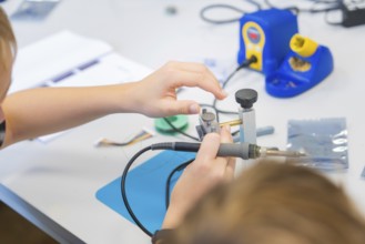 Person soldering electronic components on a workbench with a soldering iron, Youth Research Centre