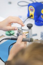 Close-up of two hands working with a soldering iron on a technical device, Youth Research Centre