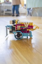Colourful Lego robot with wheels on a wooden floor demonstrates technical creativity, Youth