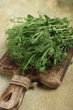 A bunch of vibrant green pea shoots lies on a rustic wooden cutting board, showcasing their