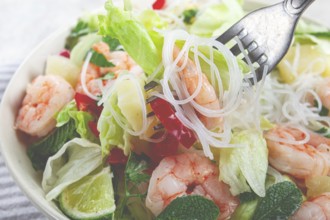 Thai salad with shrimp and rice noodles, pineapple slices, coriander and mint leaves, on a white