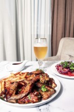 Delicious barbecue chicken wings, with French fries, salad and a refreshing drink, at a cozy table,