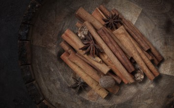 Cinnamon sticks, with nutmeg and anise star, in a wooden plate, top view, no people