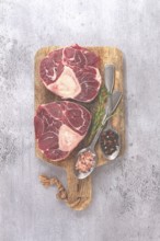 Freshly sliced beef legs, two ossobuco steaks, on a wooden board, with spices and herbs, ready to
