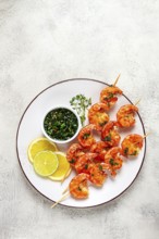 Grilled shrimp, on skewers, served with hot sauce and lime slices, on a white plate, no people