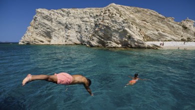 People swimming in clear blue water in front of impressive rocky cliffs, White Cliffs, White Beach,