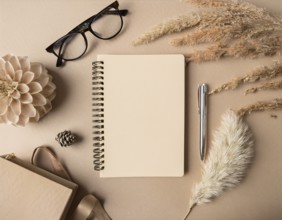 Flat lay composition featuring a beige spiral notebook, elegant pen, glasses, dried flowers, and