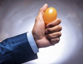 A suited hand squeezing an orange stress ball, symbolizing stress relief, productivity, and