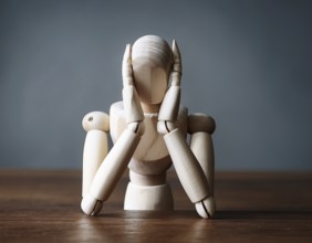 A wooden mannequin seated at a table conveys emotions of stress, thought, and contemplation.