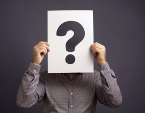 A person concealing their face while holding a question mark sign, symbolizing anonymity, mystery,