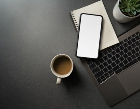 Op view of an organized workspace featuring a laptop, smartphone, notebook, pen, plant, and coffee