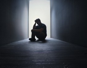 A silhouette of a person seated on the floor, conveying feelings of sadness and solitude against a