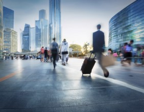 People with luggage walking on a modern city footbridge during sunset, showcasing urban life and