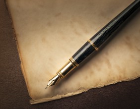 Close-up of a classic fountain pen lying atop old aged paper on a wooden surface, symbolizing