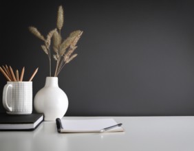 A clean and modern office workspace featuring a pen holder, notebook, and ceramic vase against a