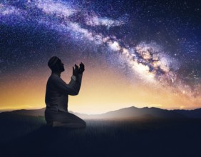 A man kneels in peaceful reflection under the vibrant Milky Way galaxy at sunset in an open natural