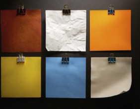 An arrangement of colorful square paper sheets held by binder clips, placed on a dark surface,