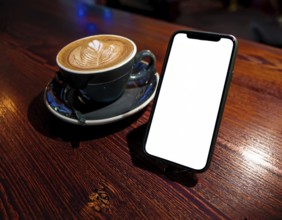 A sleek mobile phone placed near a cup of coffee, set against a blurred, warm glowing lights