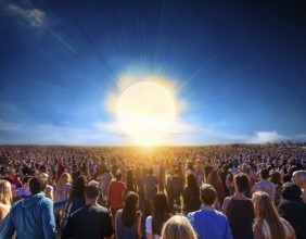 A group of individuals walks along the ground, silhouetted by a large setting sun, creating a