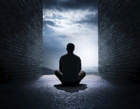 Silhouette of a person sitting alone within a brick archway, observing a peaceful and scenic cloudy