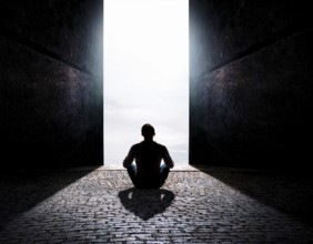 Silhouette of a person sitting alone within a brick archway, observing a peaceful and scenic cloudy