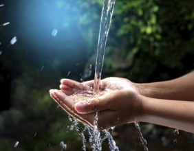 A pair of human hands collecting fresh water flowing from a source, surrounded by grassy landscape,
