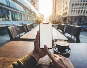 A person holding a smartphone at an outdoor cafe amidst a vibrant and lively urban setting. The
