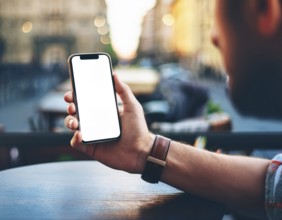 A person holding a smartphone at an outdoor cafe amidst a vibrant and lively urban setting. The