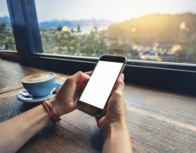 A person holding a smartphone at an outdoor cafe amidst a vibrant and lively urban setting. The