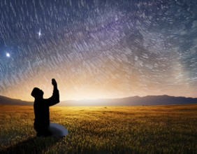 A man kneels in peaceful reflection under the vibrant Milky Way galaxy at sunset in an open natural