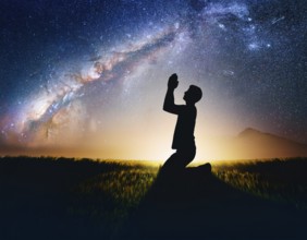 A man kneels in peaceful reflection under the vibrant Milky Way galaxy at sunset in an open natural