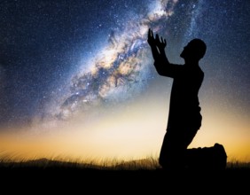 A man kneels in peaceful reflection under the vibrant Milky Way galaxy at sunset in an open natural