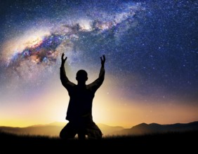 A man kneels in peaceful reflection under the vibrant Milky Way galaxy at sunset in an open natural