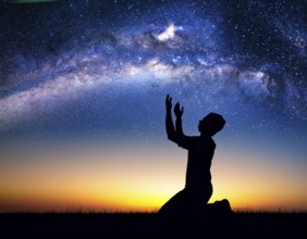 A man kneels in peaceful reflection under the vibrant Milky Way galaxy at sunset in an open natural
