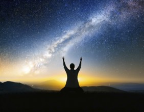A man kneels in peaceful reflection under the vibrant Milky Way galaxy at sunset in an open natural