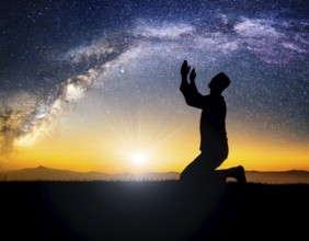 A man kneels in peaceful reflection under the vibrant Milky Way galaxy at sunset in an open natural