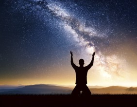 A man kneels in peaceful reflection under the vibrant Milky Way galaxy at sunset in an open natural