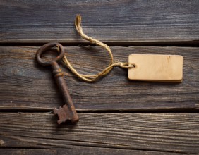 A close-up of an ornate vintage key with a blank label attached, resting on a brown surface under