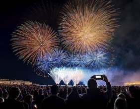 Thrilling fireworks illuminate the dark sky as a crowd gathers to enjoy the dazzling display,